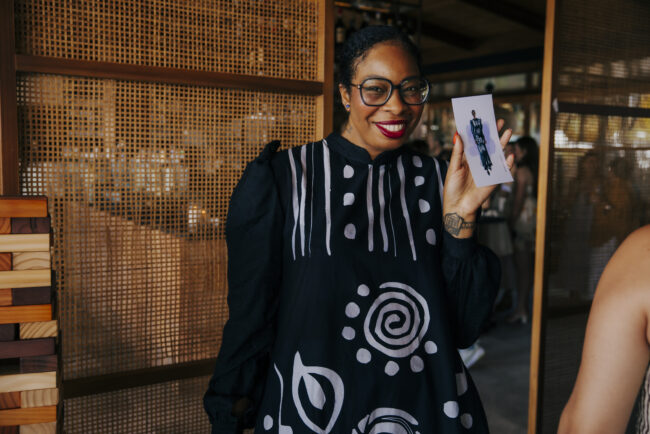 Guest holding her custom fashion sketch at the Savage X Fenty summer party in Santa Monica